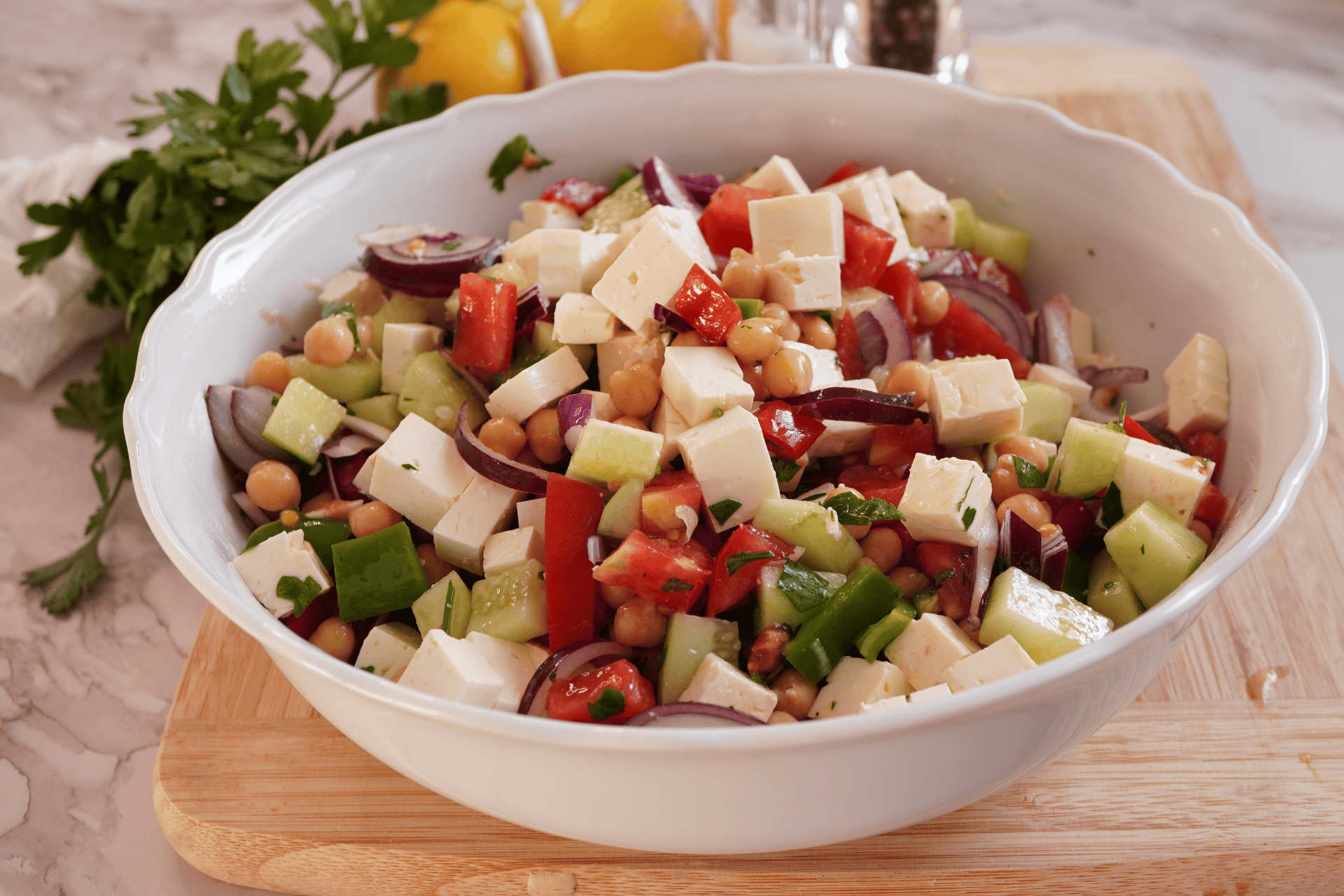 Marinated chickpea salad in a white bowl with cucumber, tomato, red onion and cubed feta