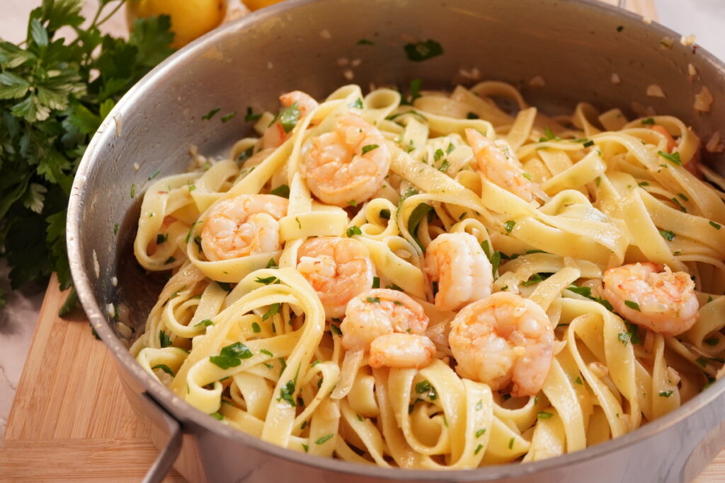 Garlic butter shrimp pasta in a pan, topped with seared shrimp and fresh parsley on the side