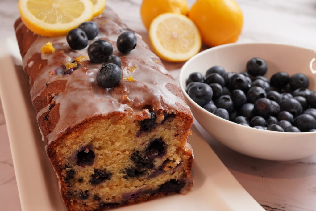 Sliced lemon blueberry loaf with lemon glaze and fresh blueberries on top
