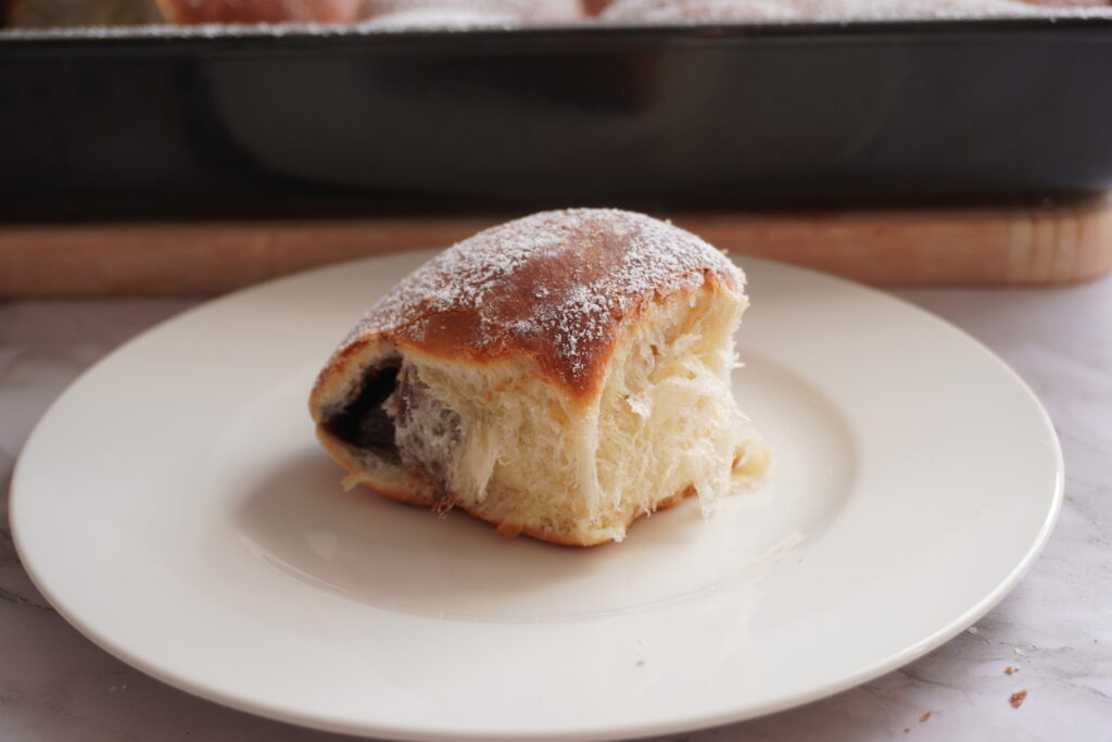 Single Nutella Buchtel with a golden-brown top dusted with powdered sugar, Nutella peeking out and a soft, fluffy crumb